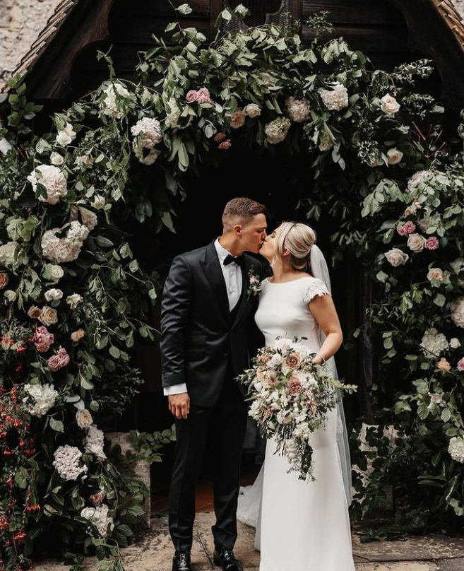 Image of bride and groom kissing in front of a floral archway | Wedding flowers